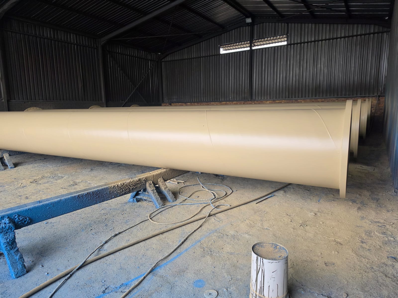 Long coated steel pipe spools on fabrication stands inside the Wetpipe workshop